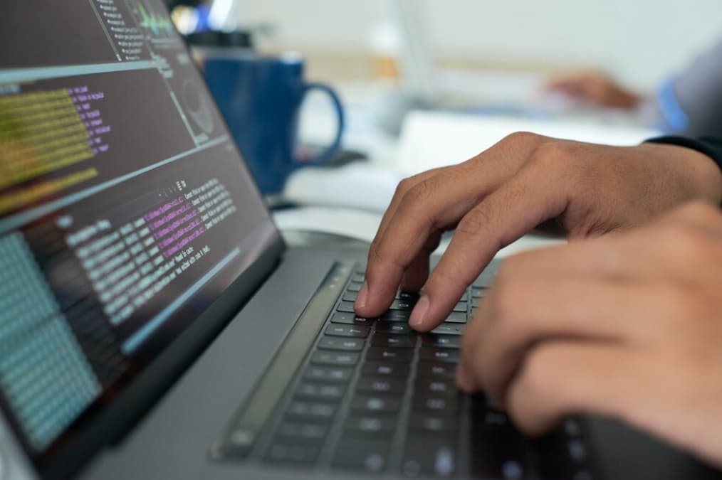 Close-up of a person's hands typing code on a laptop